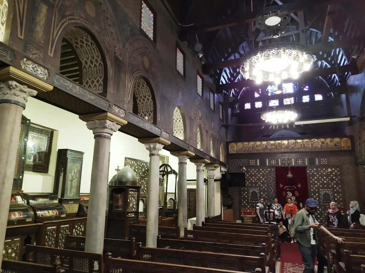 The interior of an old Coptic church: rows of marble columns, dark wooden screens inlaid with ivory, and hanging lamps.