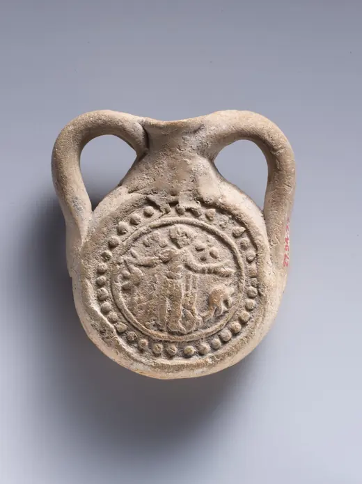 A small round clay flask with two handles, stamped with a standing figure between two animals inside a beaded circle.