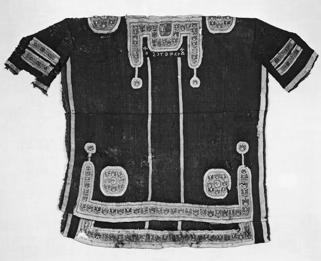 An ancient linen tunic with woven decorative panels, laid flat.