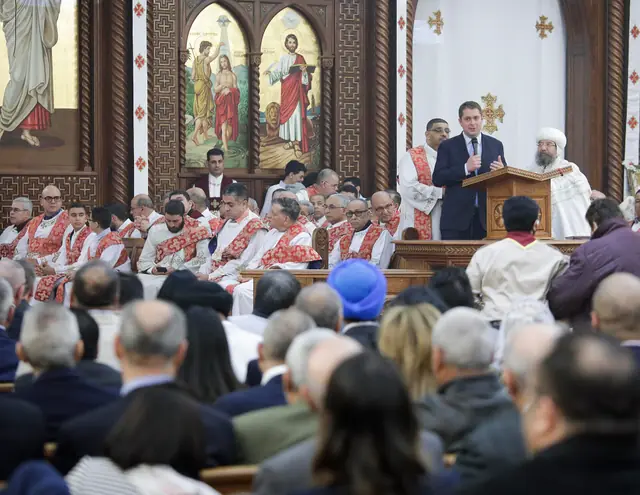 Rows of deacons seated in white tunics with red embroidered stoles over the left shoulder.
